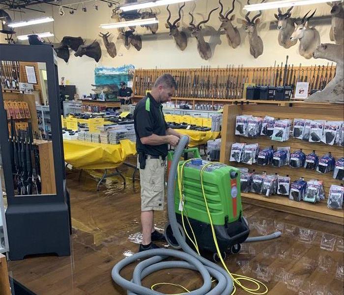 Hunting Gun Range Store flooded floor, man with green equipment and hose, mounts on wall